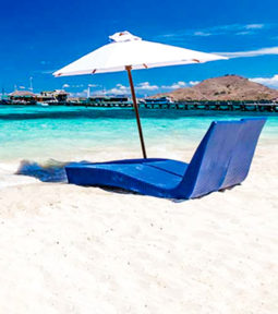 Two blue chairs and a white umbrella on white sand beach