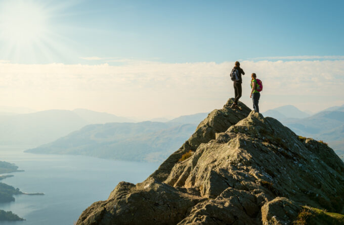Two female hikers on top of the mountain enjoying valley view, Ben A'an, Loch Katrina, Highlands, Scotland, UK