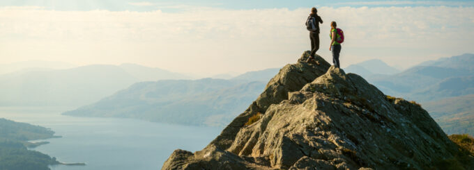 Two female hikers on top of the mountain enjoying valley view, Ben A'an, Loch Katrina, Highlands, Scotland, UK