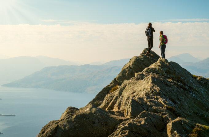 Two female hikers on top of the mountain enjoying valley view, Ben A'an, Loch Katrina, Highlands, Scotland, UK