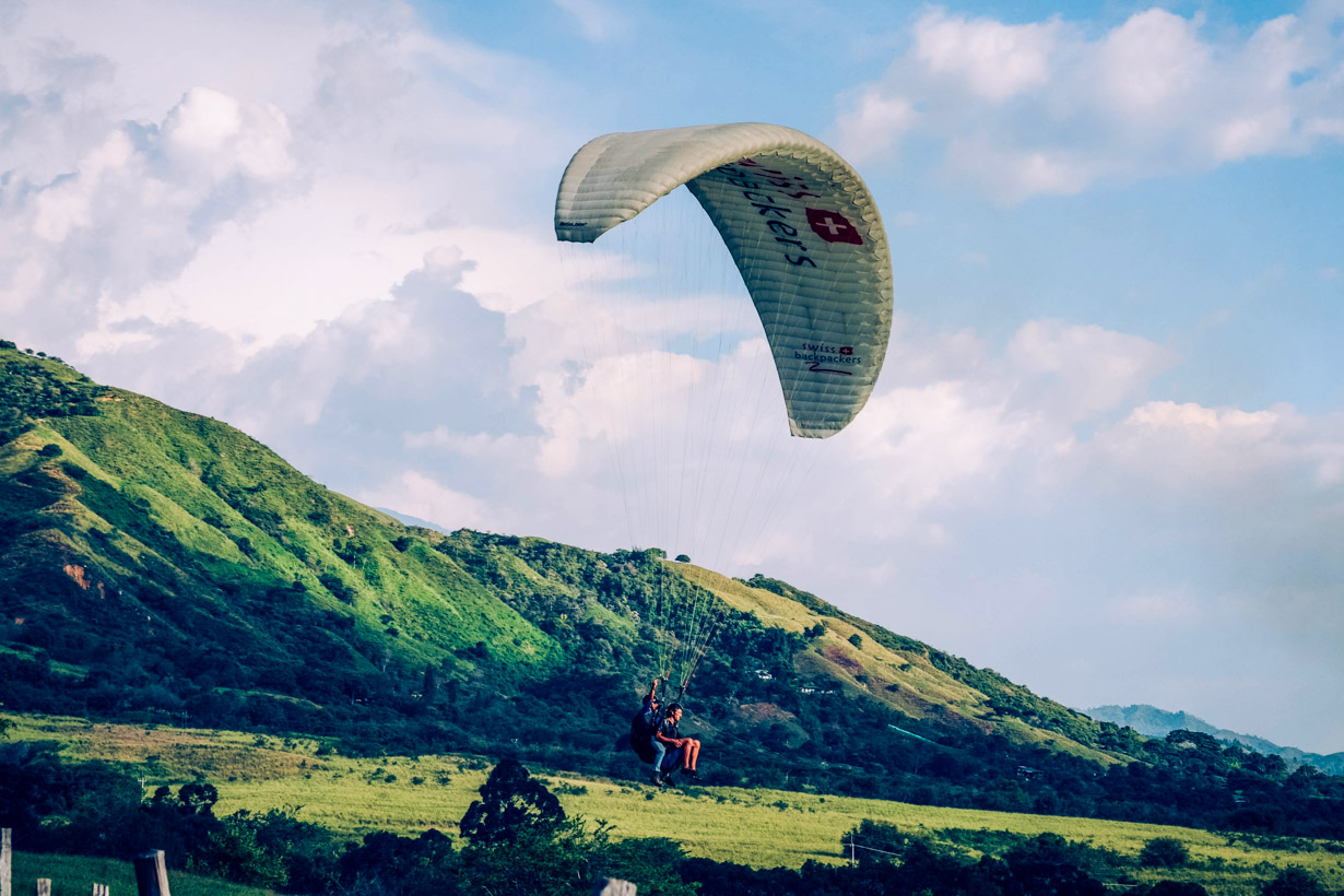 Two people paraglide near green hills in Colombia